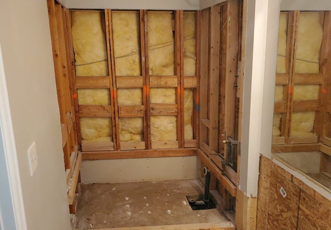 Before: the bathroom gutted to the studs, with insulation and plumbing exposed